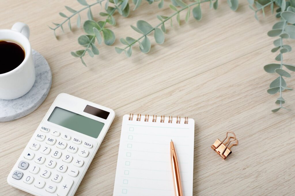 Calculator with coffee cup and notebook on light wood desk