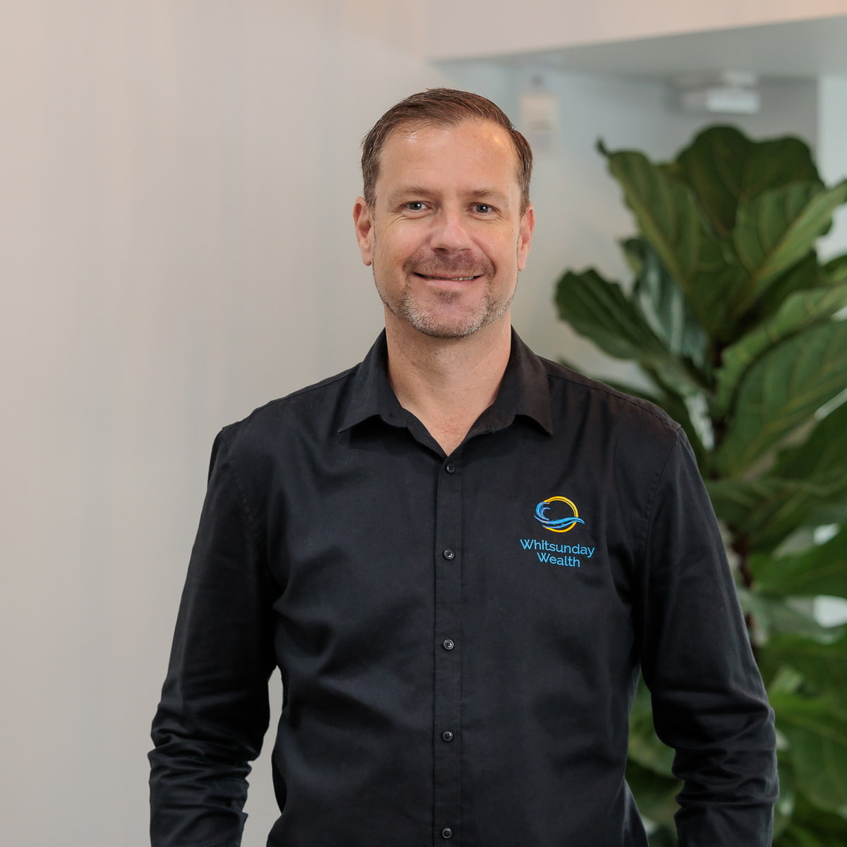 Professional headshot of Alister with plant in background
