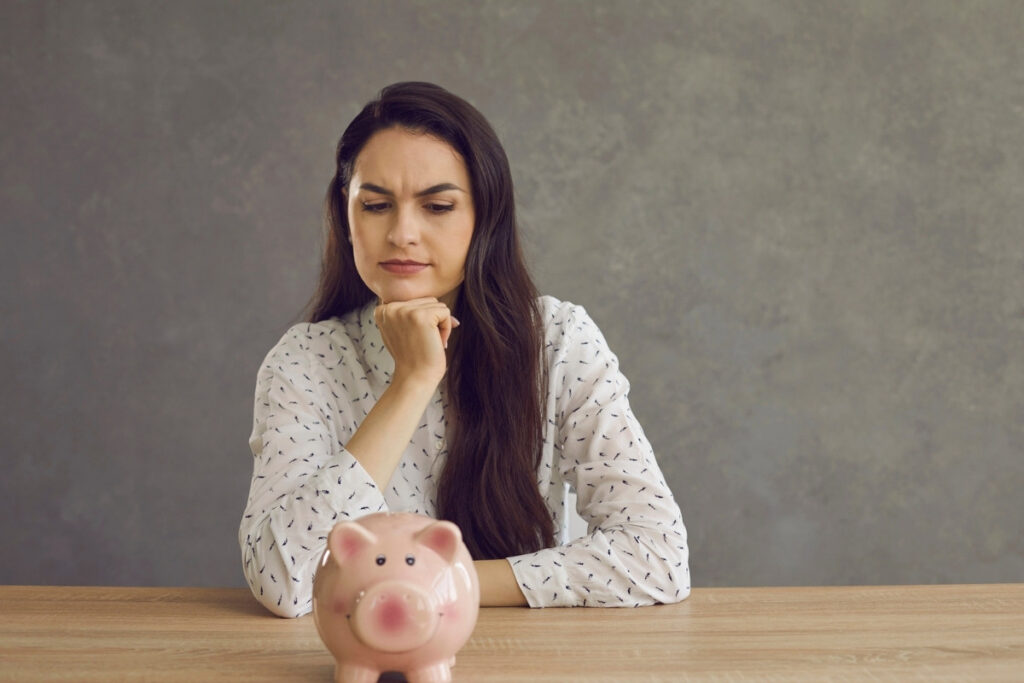Woman sitting at a table staring at a piggy back and wondering about investing