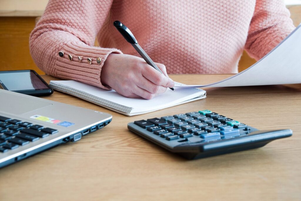 woman seated at a desk, focused on writing and using a calculator