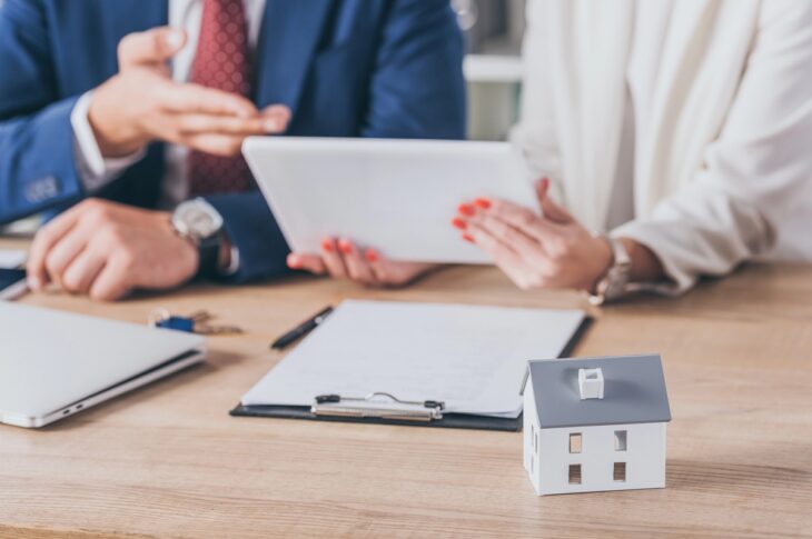 a client and a real estate agent discuss home buying, with paperwork and a house model on the table